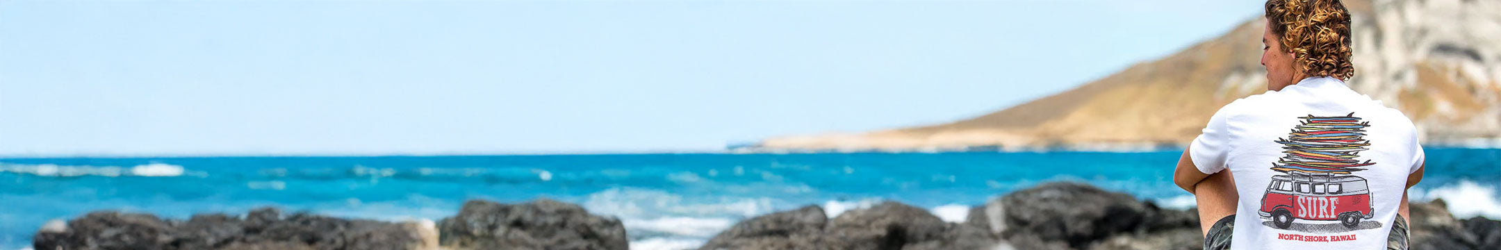 Person sitting on rocks by the ocean with a scenic view.
