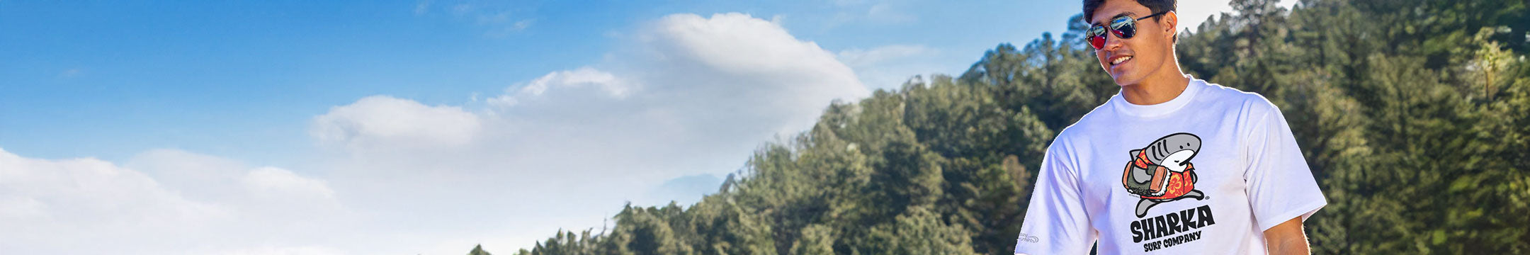 Person wearing a white t-shirt with text and graphics, standing outdoors with mountains in the background.
