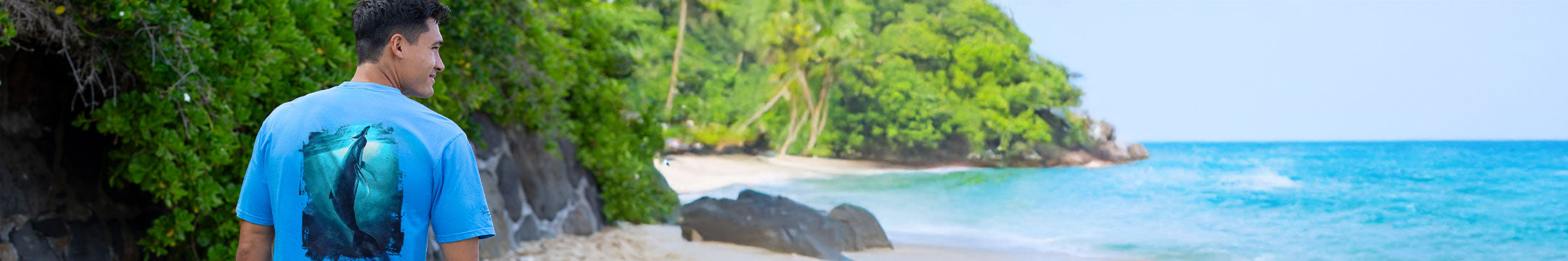 Person wearing a blue shirt with a shark design standing on a tropical beach.