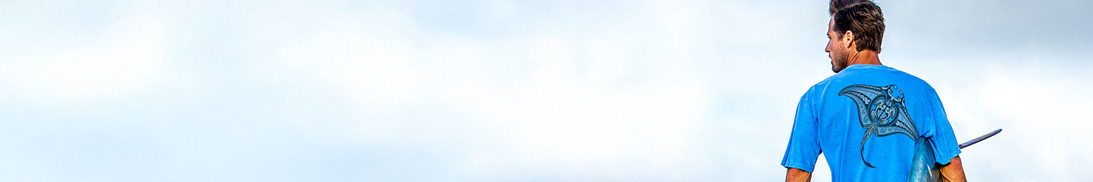 Man wearing a blue t-shirt with a graphic design, standing against a light blue sky.