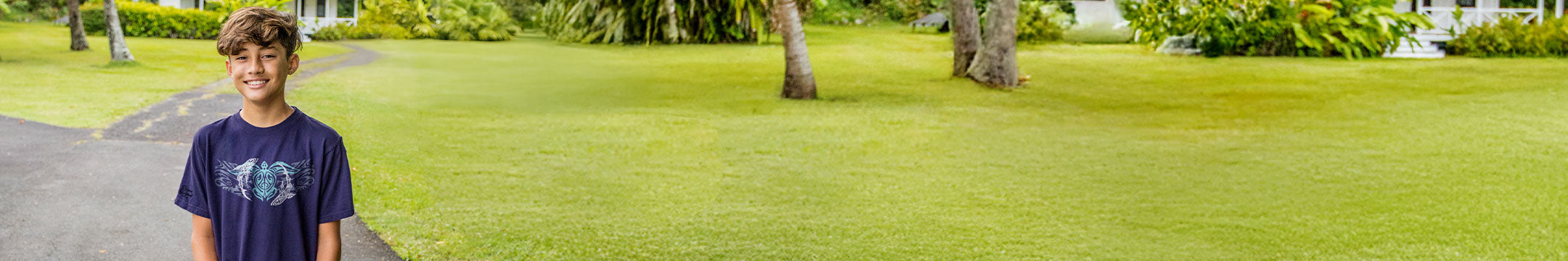 Young boy standing on a grassy area with trees in the background