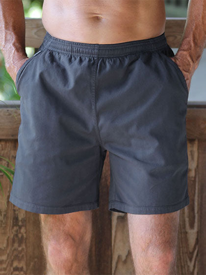 A close-up of a man wearing dark gray shorts, showing the waistband and front pocket details against a rustic wooden background.