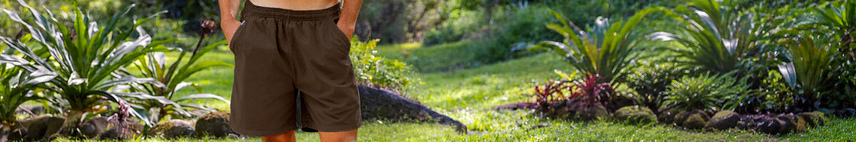 A person wearing dark brown shorts stands in a lush tropical garden with green plants and grass.