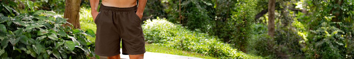 A man wearing brown shorts stands outdoors in a lush green garden setting.