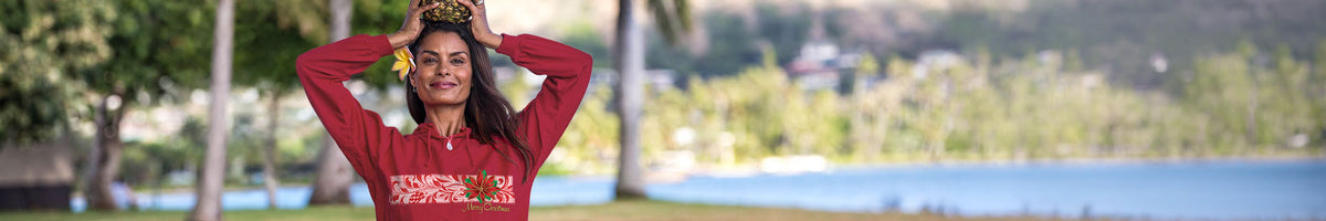 A woman wearing a red long-sleeve top with a colorful graphic print on the front, posing outdoors with a scenic lake and trees in the background.