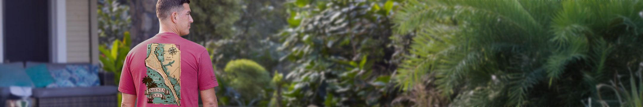 Person wearing a Paradise red shirt with a graphic design, standing outdoors near greenery.