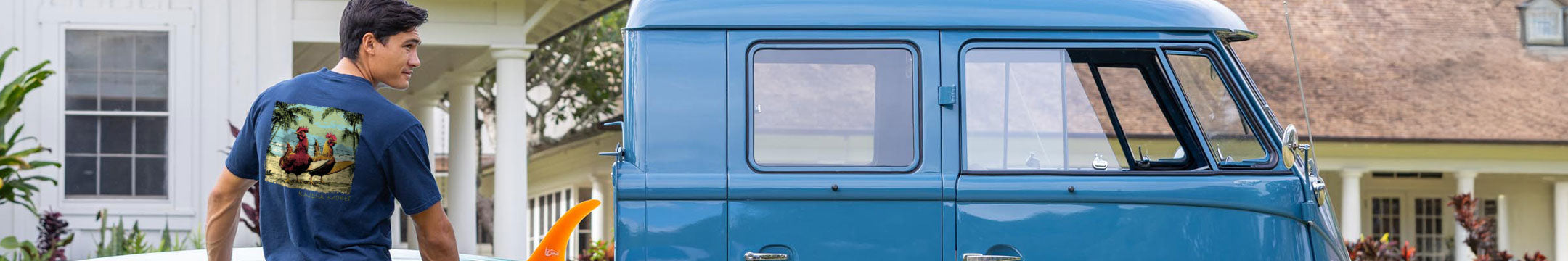 Man wearing a blue t-shirt with a graphic design, standing next to a vintage blue van.