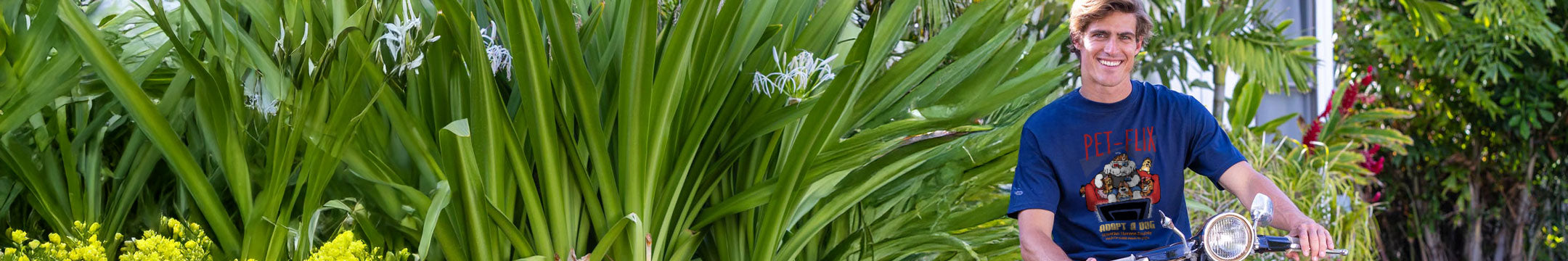 a man wearing an adopt a dog tee riding a bicycle among green plants