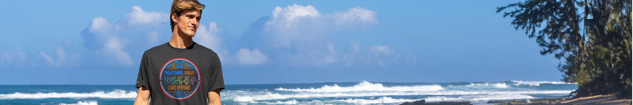 Person wearing a black t-shirt with a colorful graphic design by the ocean.