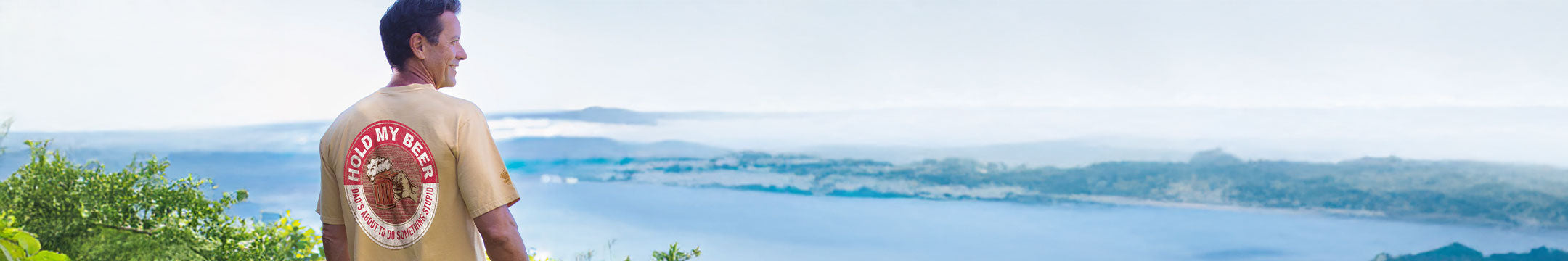 Person wearing a yellow shirt with a logo, standing on a scenic overlook.
