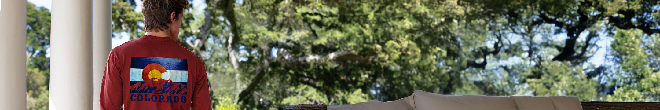 Person wearing a red long sleeve shirt with a Colorado design, standing outdoors with trees in the background