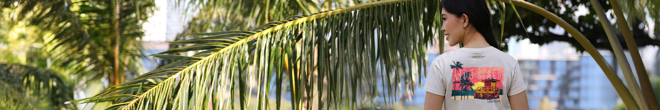 Woman standing outdoors with palm leaves and blurred background wearing a lindo beach shirt