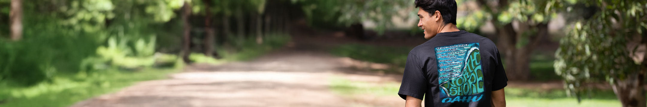 Person wearing a black t-shirt with a Oahu Hawaii graphic design, standing on a path in a forest.