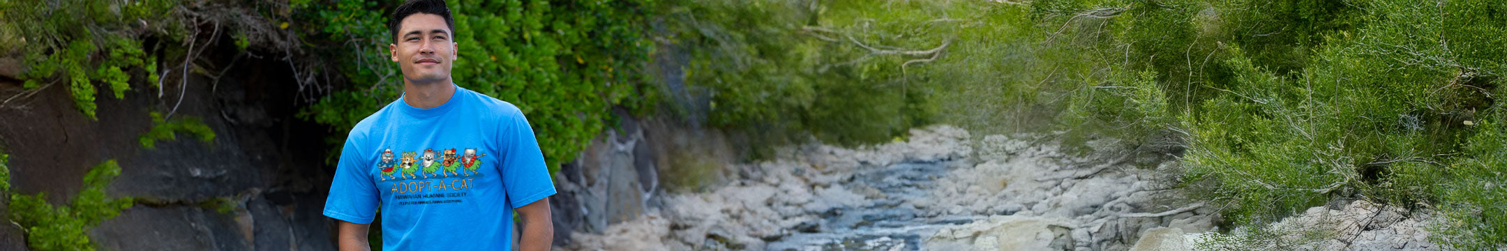 Man in a blue shirt standing near a stream with greenery