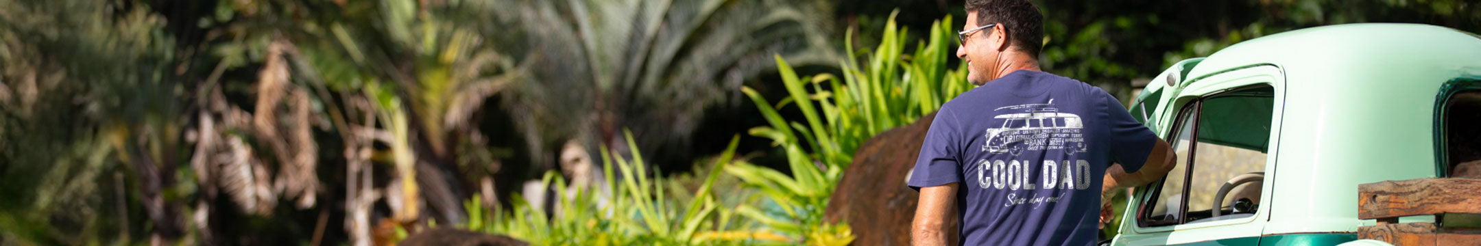Man standing next to a vehicle in a tropical setting with palm trees.