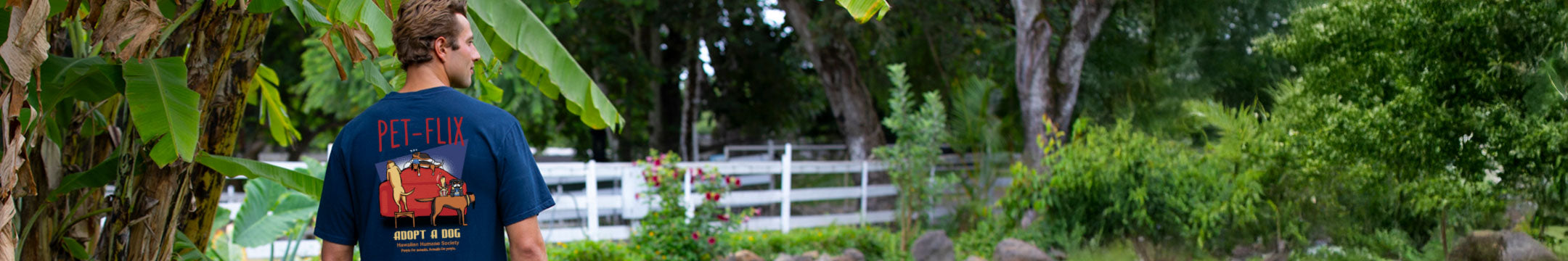 Man wearing a blue adopt a dog shirt 
standing in a lush green garden.
