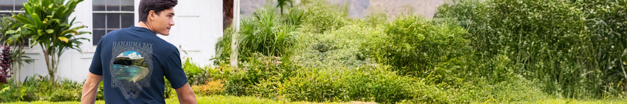 Person walking through a garden with greenery and plants wearing a navy crazy shirt with a Ocean design 