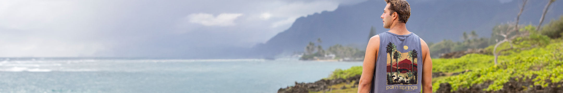 Man standing on a beach with a scenic view of mountains and ocean.