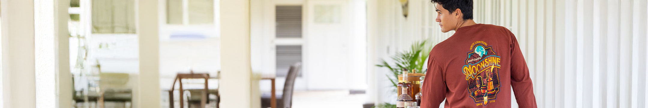 Person wearing a whiskey dyed long-sleeve shirt with a beverage graphic design in a home setting