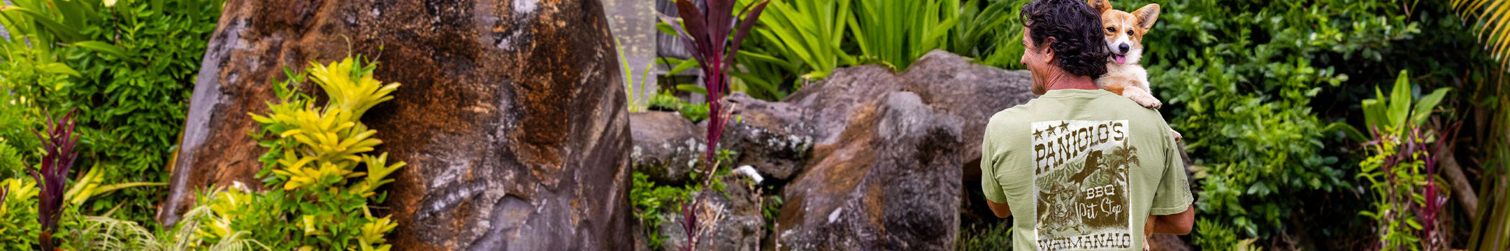 Person holding a dog in a lush green forest setting wearing a funny crazy shirt