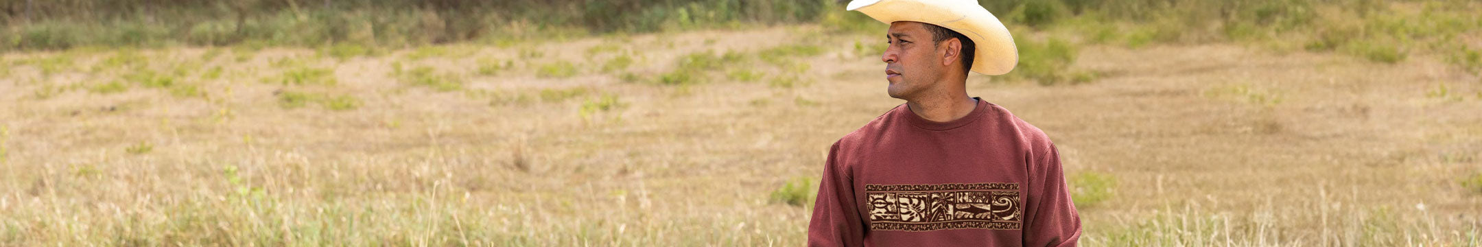 Man wearing a cowboy hat and shirt with a linear design standing in a field
