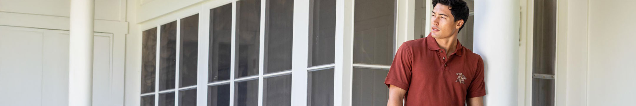 Man standing in front of a large windowed door, wearing a whiskey dyed polo shirt.