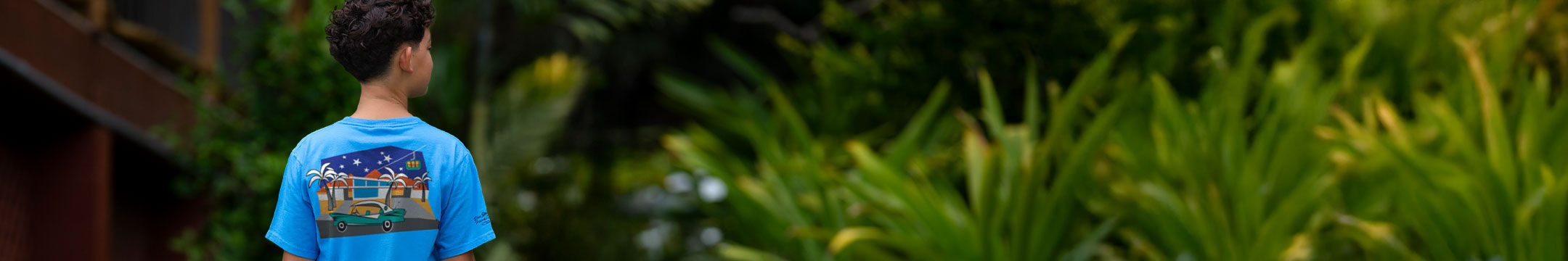Kid wearing a blue hawaii dyed t-shirt with a graphic design, standing in a natural setting with greenery.
