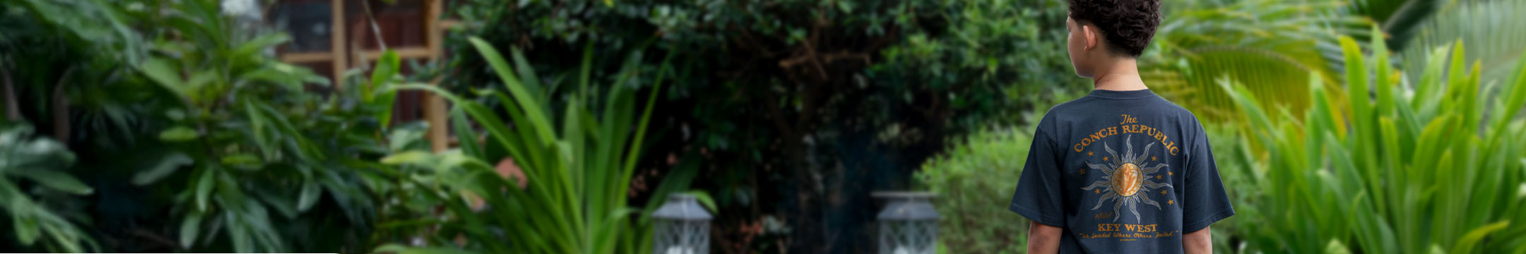 Kid wearing a dark t-shirt with a graphic design, standing in a lush green garden.