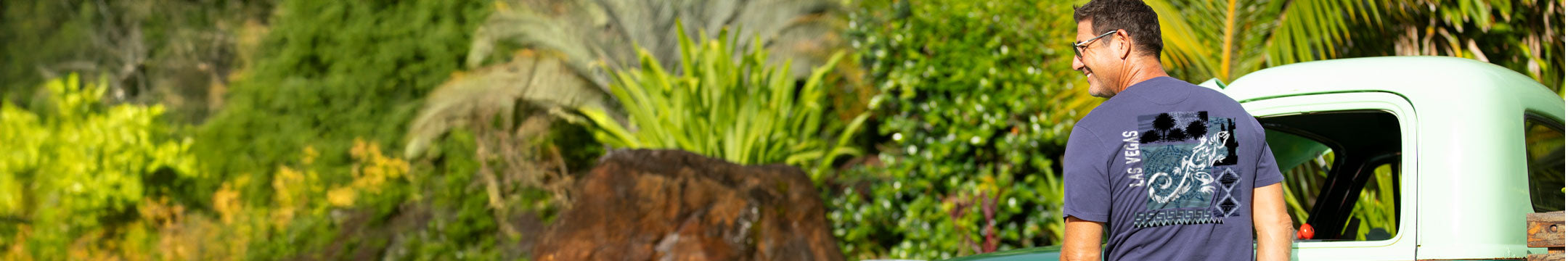 Man standing next to a car in a forested area wearing a Las Vegas Tee