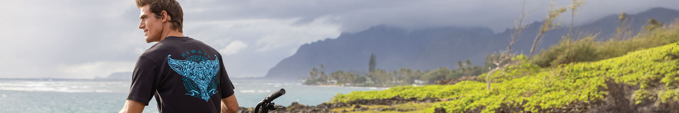 Man standing on a grassy area with a scenic ocean view and mountains in the background