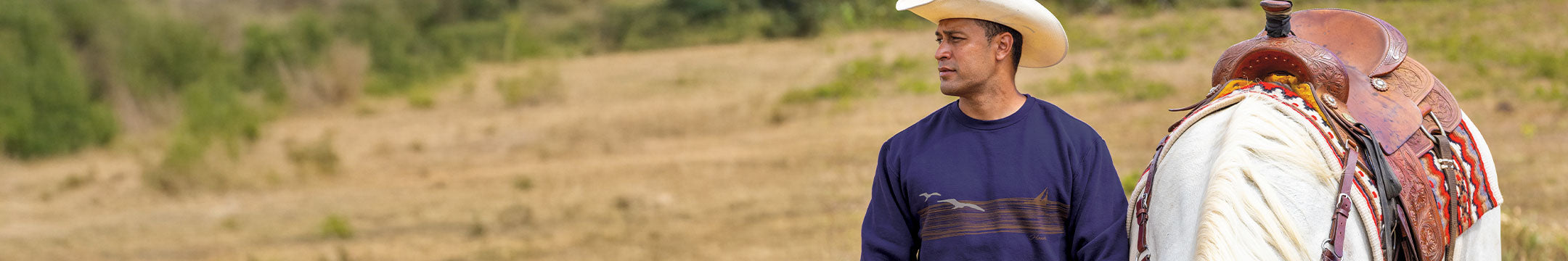 Man wearing a purple long sleeve standing outside next to a horse