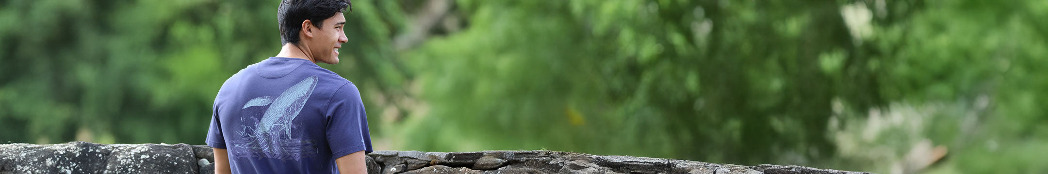Man standing outdoors with greenery and rocks in the background wearing a pima tee