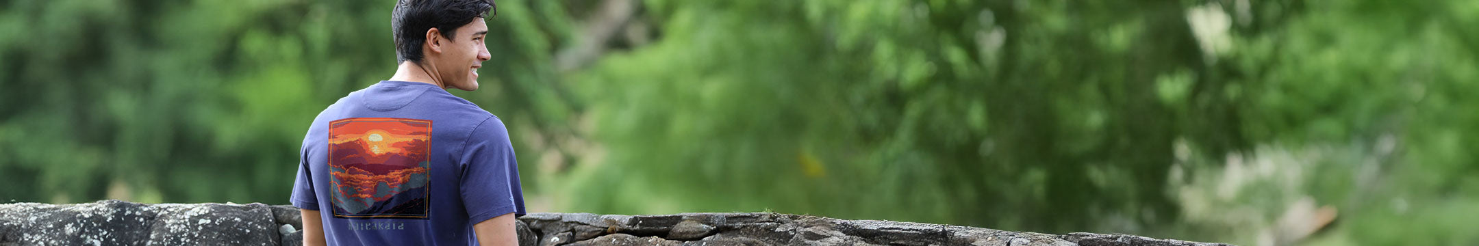 Man wearing a indigo pima tee with a sunrise design on it standing outside 