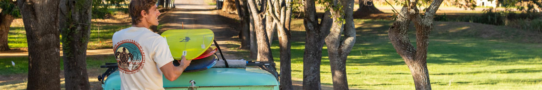 Man wearing a tan shirt with a tribal turtle design putting surfboards onto a car