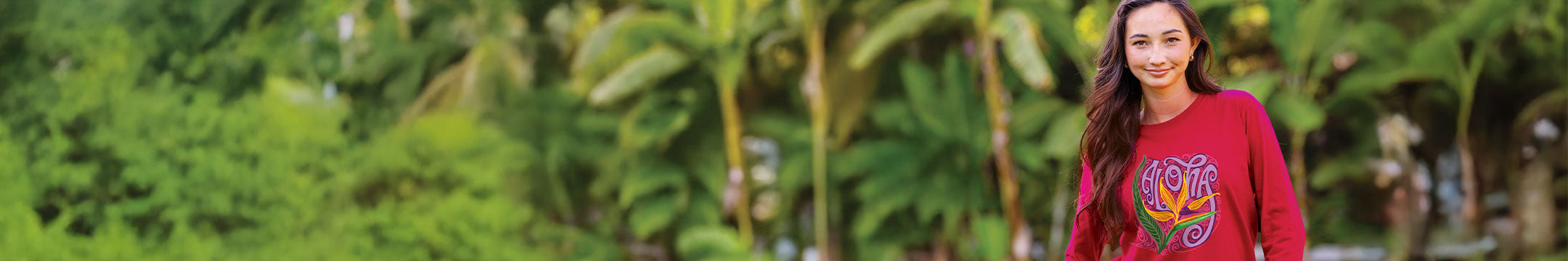 Woman wearing a red sweatshirt with a colorful design, standing in a tropical setting with palm trees.