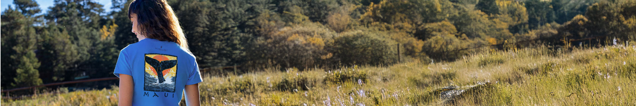 Person wearing a blue hawaii dyed t-shirt with 'Vail' printed on it, standing in a grassy field with trees in the background