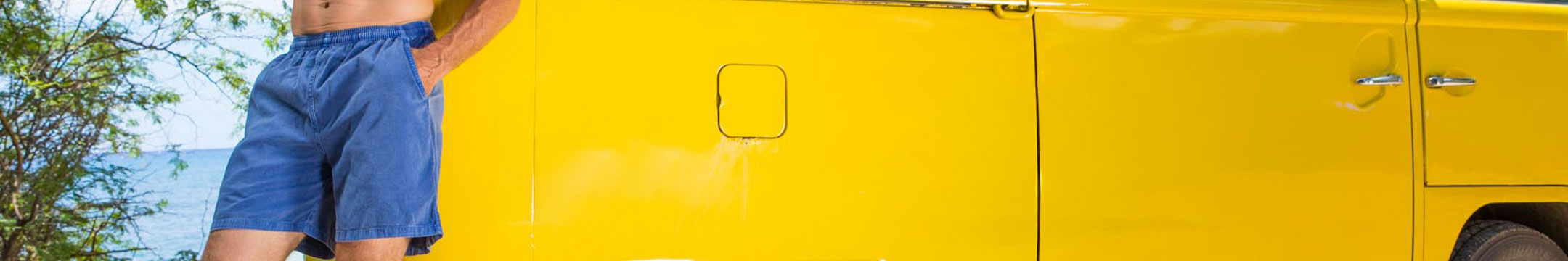 Person wearing blueberry dyed shorts standing next to a yellow vehicle by a body of water.