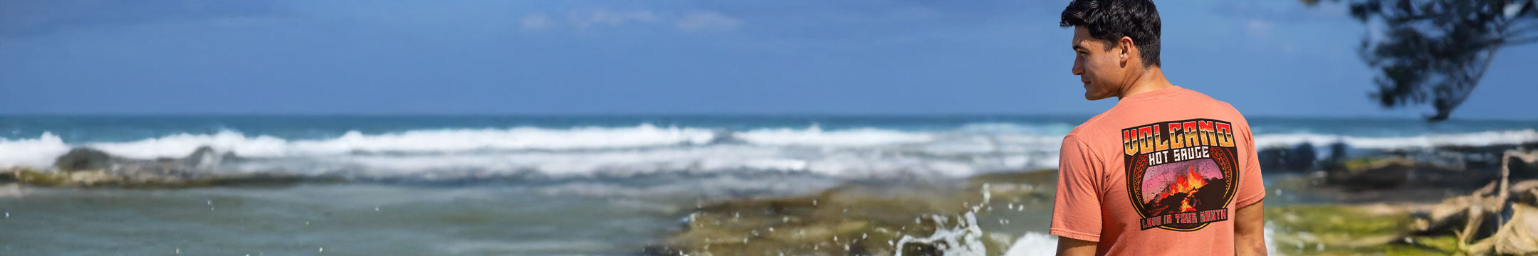 Person wearing a chile dyed  t-shirt with a graphic design, standing by the ocean with waves crashing on the shore.