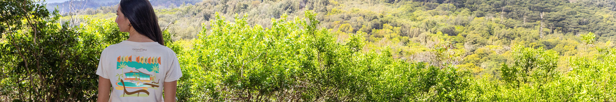 Woman wearing a Coconut dyed t-shirt with text standing in a lush green forest