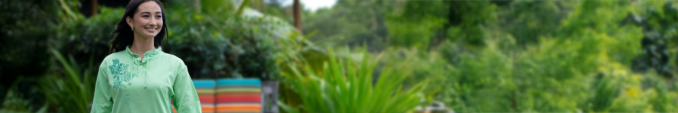 Woman in a green shirt standing in a lush green garden with colorful striped fabric in the background.