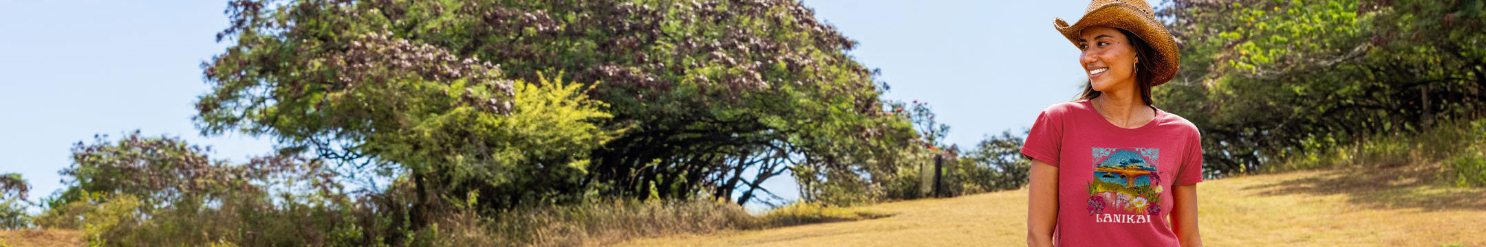 Woman wearing a paradise red t-shirt with a 'LANIKAI' design on the front - standing outside in a field 