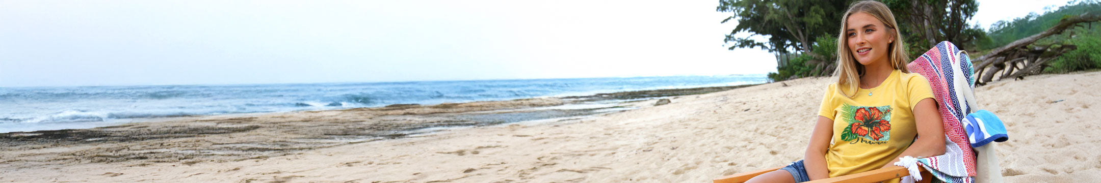 Woman sitting on a beach with a scenic ocean view wearing a pineapple dyed tee