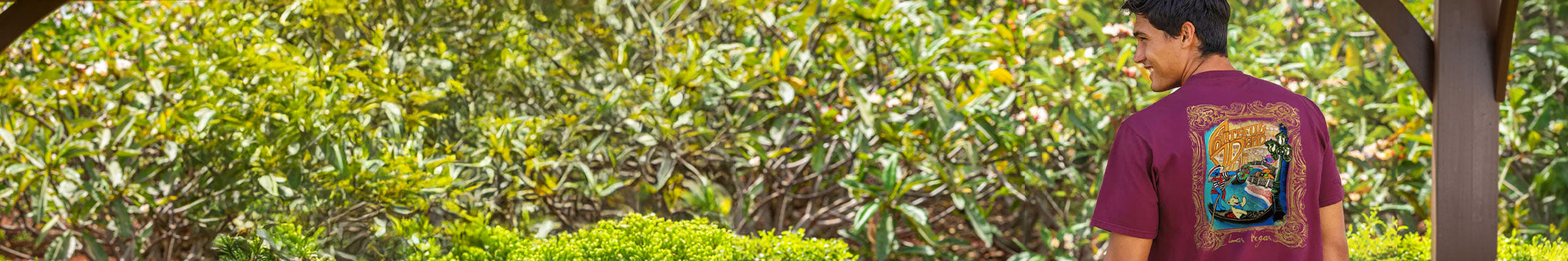 A man wearing a Wine Dyed Tshirt with a graphic design in a green outdoor setting
