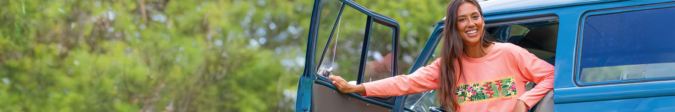 Woman standing next to a blue vehicle with a floral pattern on a blurred natural background