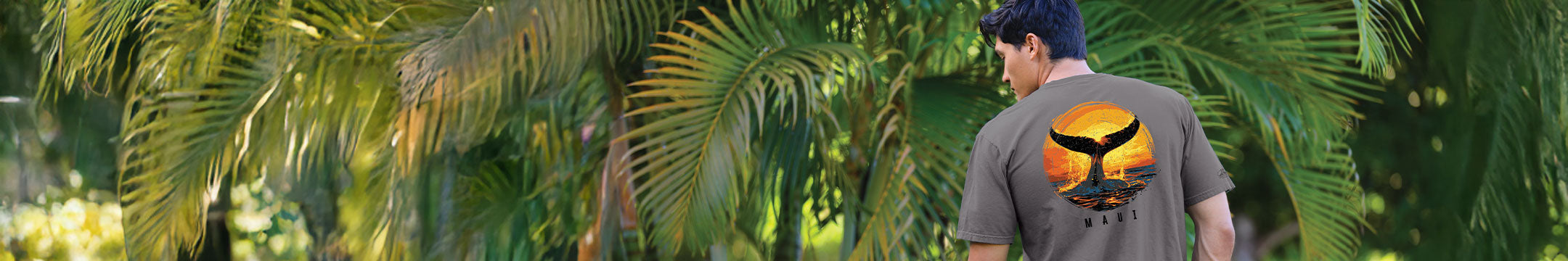 Person wearing a gray t-shirt with a logo walking through a tropical setting with palm trees.