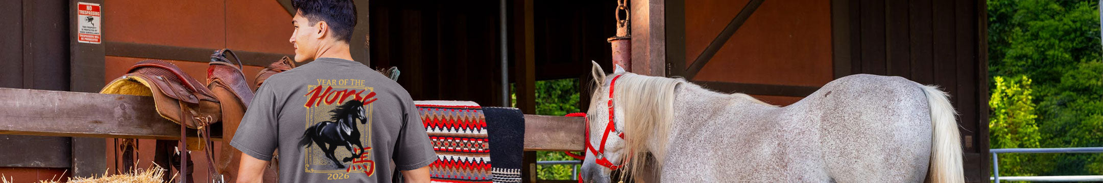Man standing next to a white horse with a red bridle in front of a wooden stable.