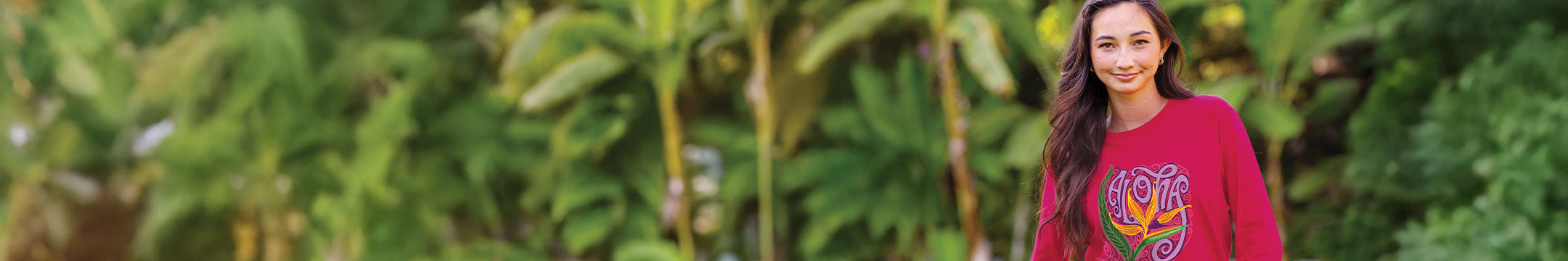 Woman wearing a raspberry dyed long sleeve with an aloha floral design on the front with a tropical background