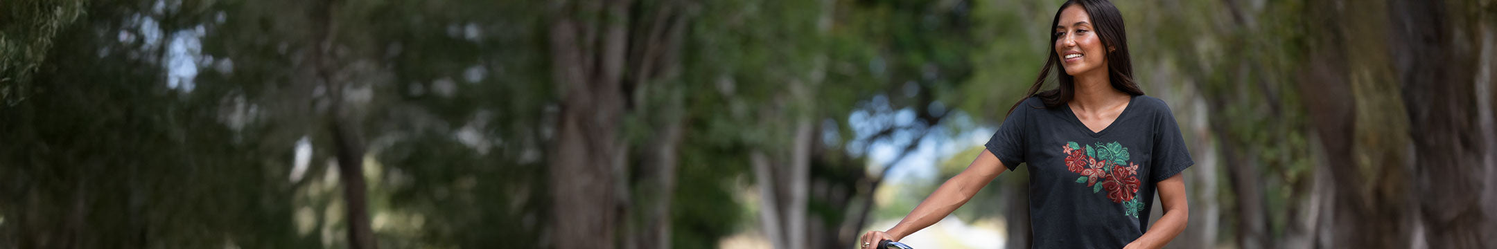 Woman standing outside holding the handlebars of a bike wearing  a black v-neck tee with a floral design on the front