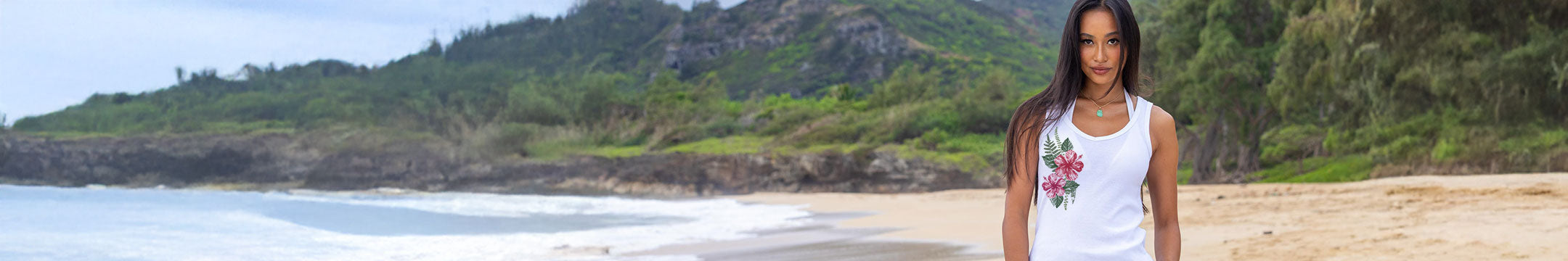 Woman standing on a beach with greenery and ocean in the background