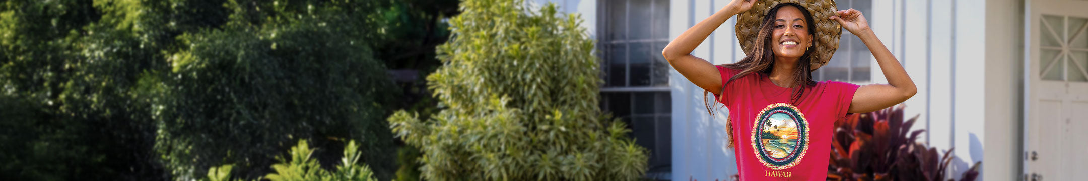 Woman wearing a raspberry dyed t-shirt with a graphic design, standing outdoors with greenery and a building in the background.